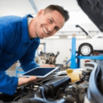 meccanico sorridente in maglia blu elettrico controlla il cofano di un'auto