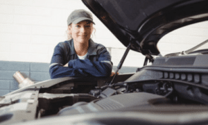 una donna meccanico con cappellino appoggiata ad un auto con cofano aperto