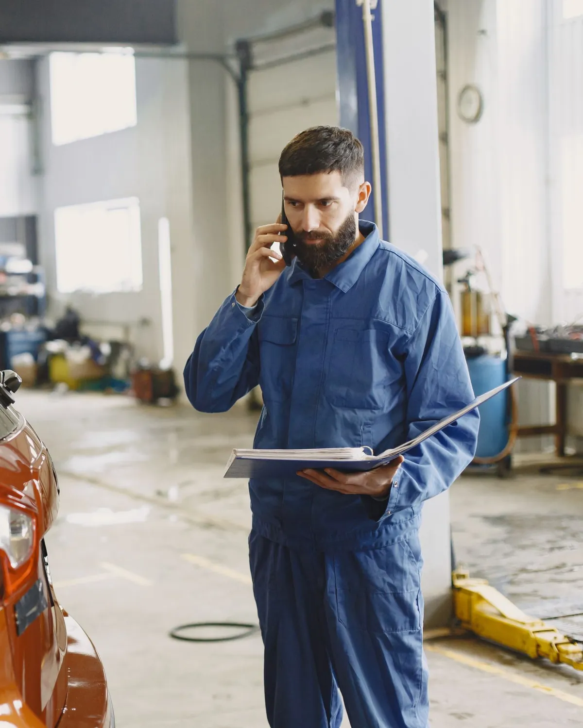 Meccanico al telefono con il cliente, accanto all'auto in officina