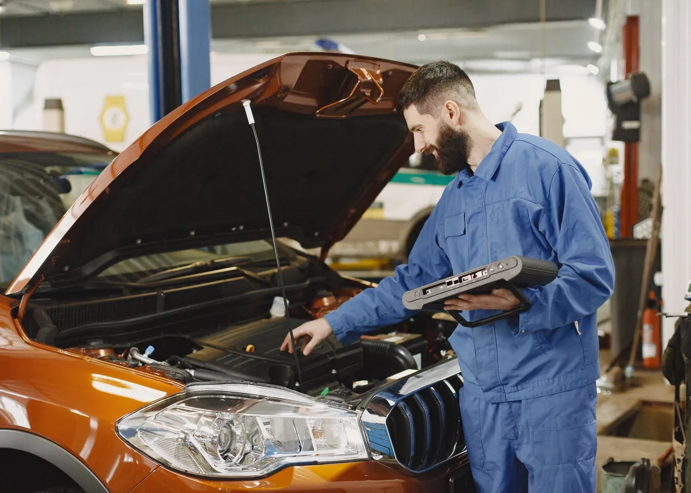 Meccanico al lavoro sotto il cofano aperto di un'auto, con lo strumento di diagnosi
